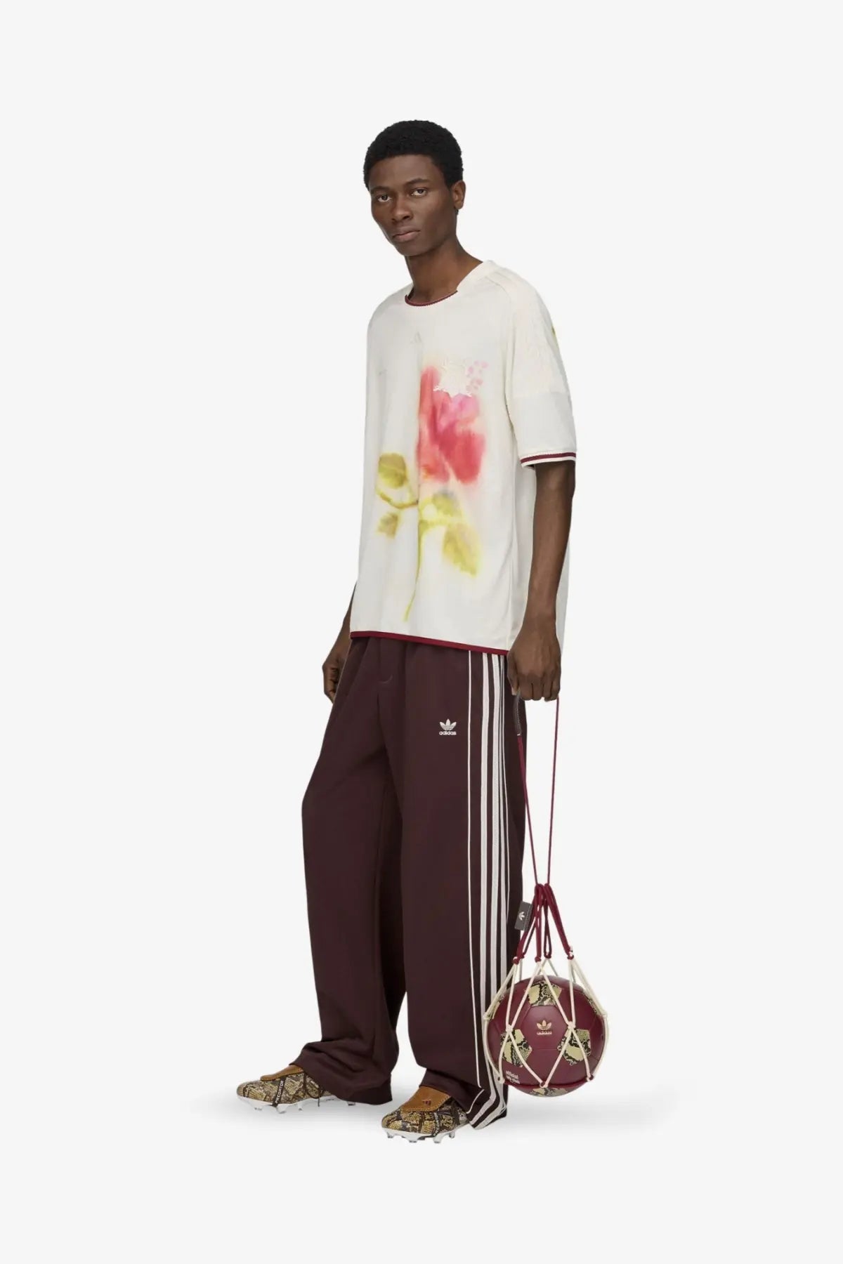 Maroon adidas basketball in a white drawstring mesh net bag alongside brown adidas originals by wales bonner recycled track trousers