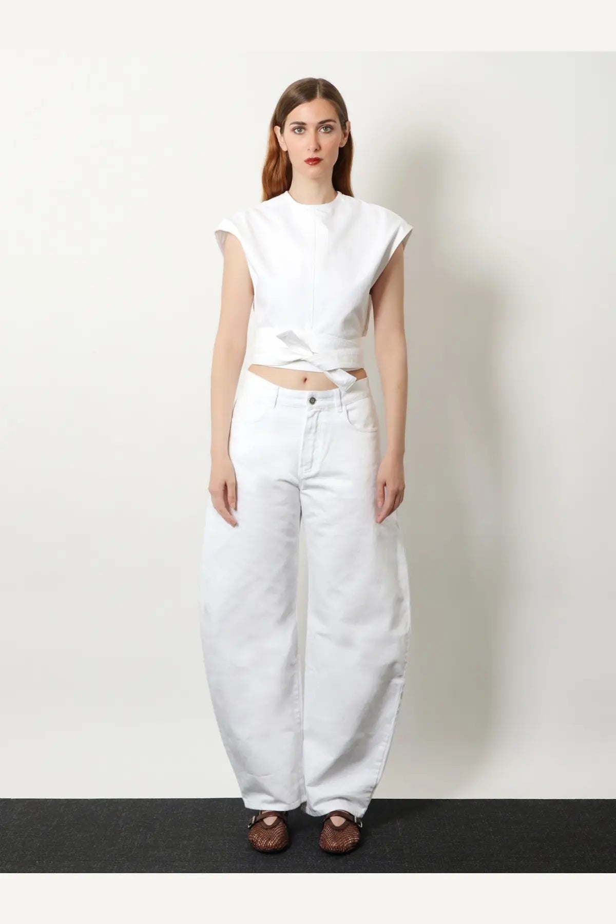 Alaïa women’s white cotton sleeveless cropped top with front tie detail paired with high-waisted white denim pants