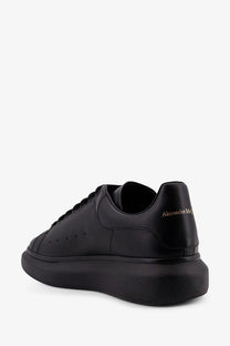 Back view of alexander mcqueen men’s black leather sneaker with chunky sole and gold branding on the heel