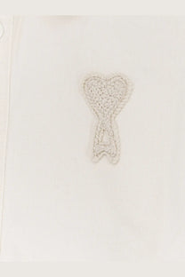 A delicate light gray crocheted heart emblem stitched on the white cotton fabric of ami paris men’s ami de coeur shirt