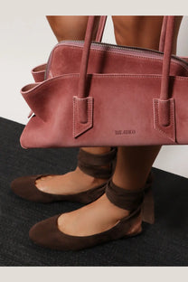 A dusty rose suede handbag with structured rectangular shape two top handles and embossed brand logo on front