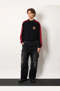 Balenciaga men’s black denim cargo trousers paired with black and red color-blocked sweatshirt with chest patch