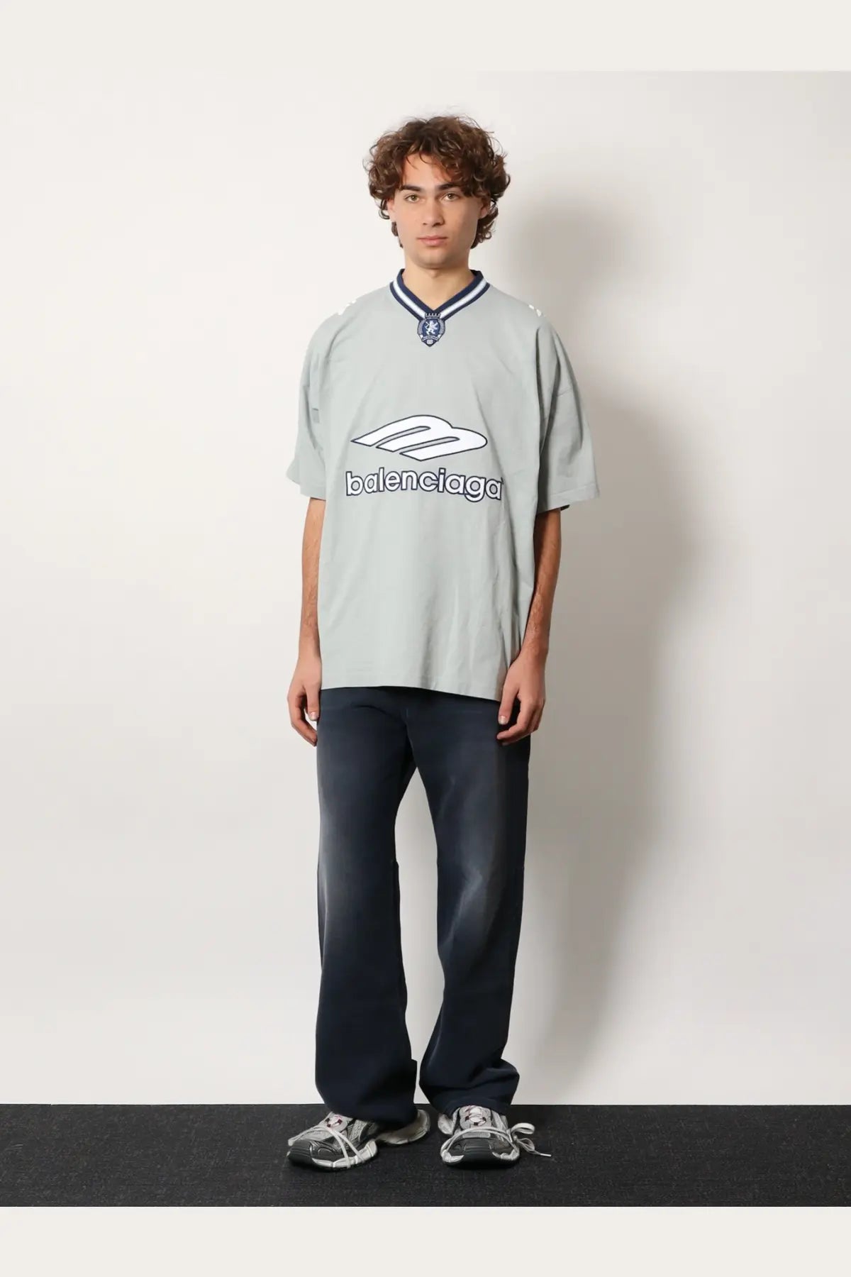 Light gray balenciaga oversized cotton t-shirt with white logo and navy blue collar trim paired with blue men’s jeans