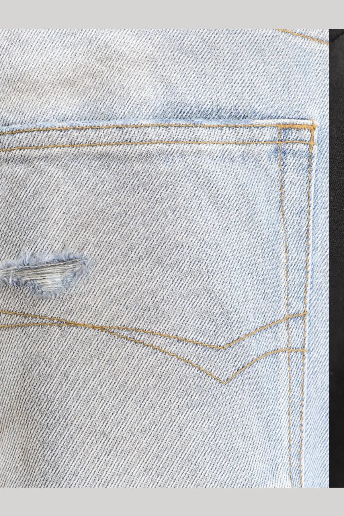 Balenciaga men’s distressed light-wash denim jeans pocket with frayed tear and contrasting tan stitching back side