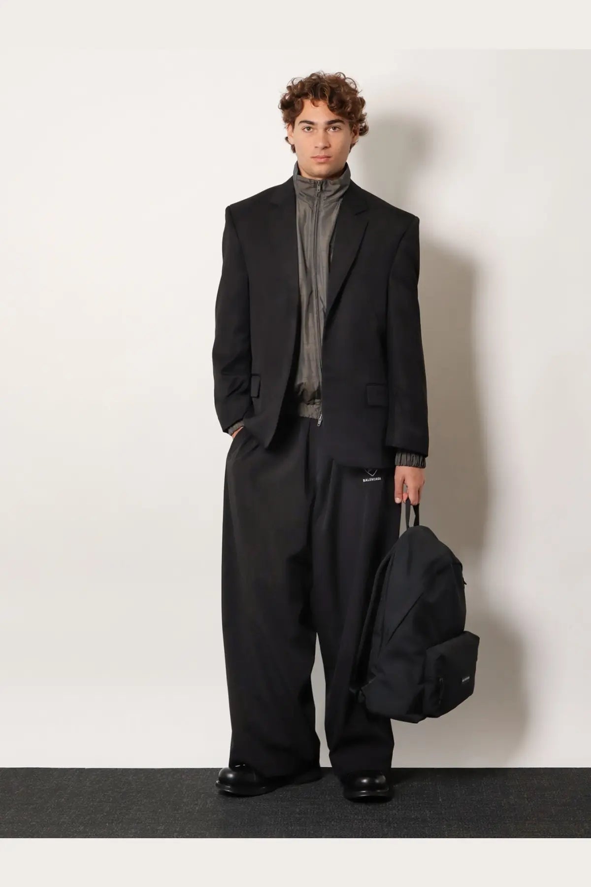 Black backpack with subtle branding and structured minimalist design paired with Balenciaga men’s madras nylon jacket grey