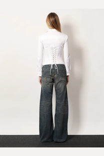 Back view of white lace-up corset style top with long sleeves paired with balenciaga curved waist blue jeans