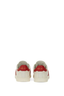 White leather bally women’s tyger sneaker with red accents and gold branding on the heel shown from the back side