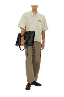 Black crocodile-embossed leather satchel bag paired with Bottega Veneta men’s beige cargo pants