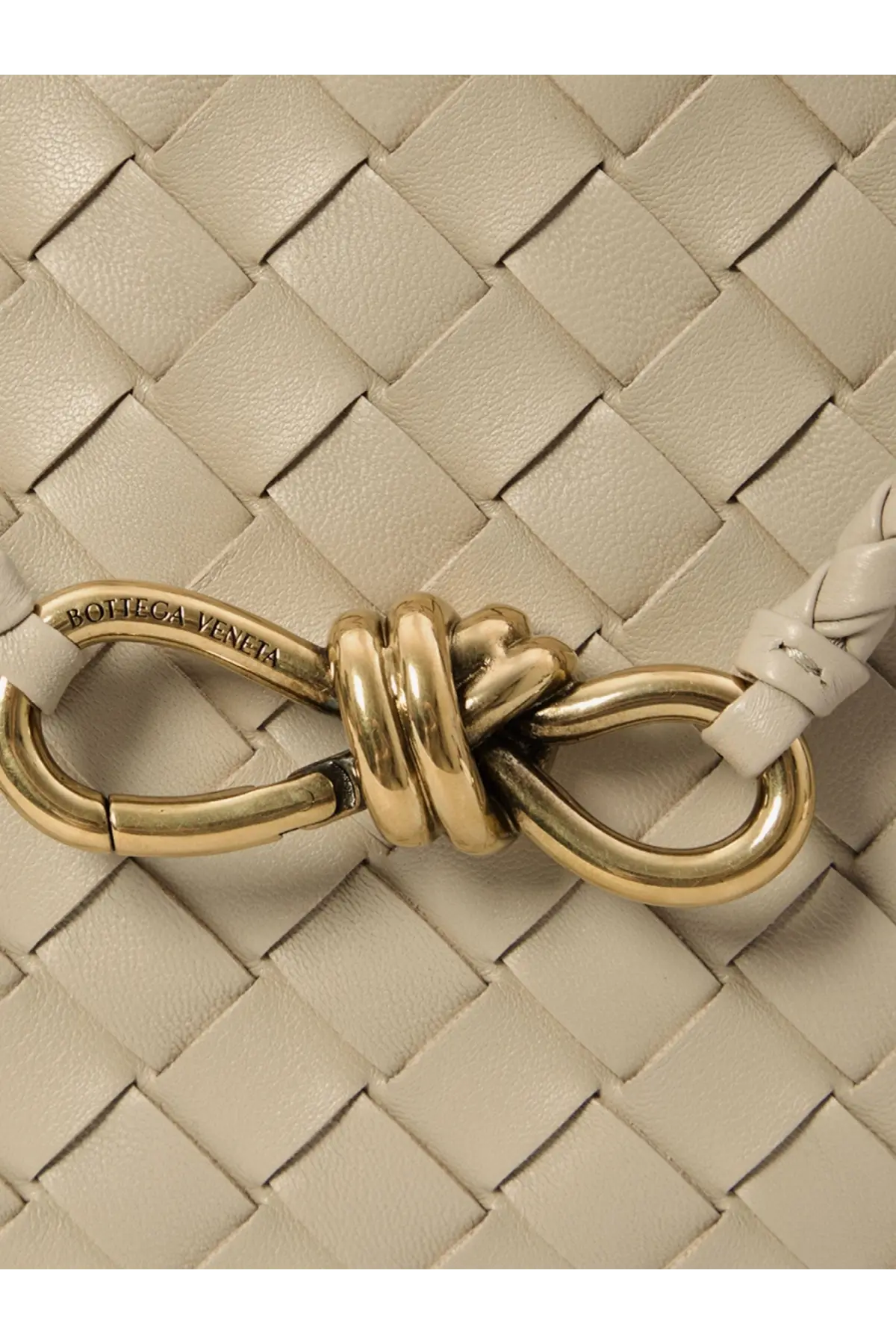 A gold tone metal clasp with knotted design engraved with bottega veneta on a light beige woven leather strap of bottega veneta womens andiamo leather shoulder bag white