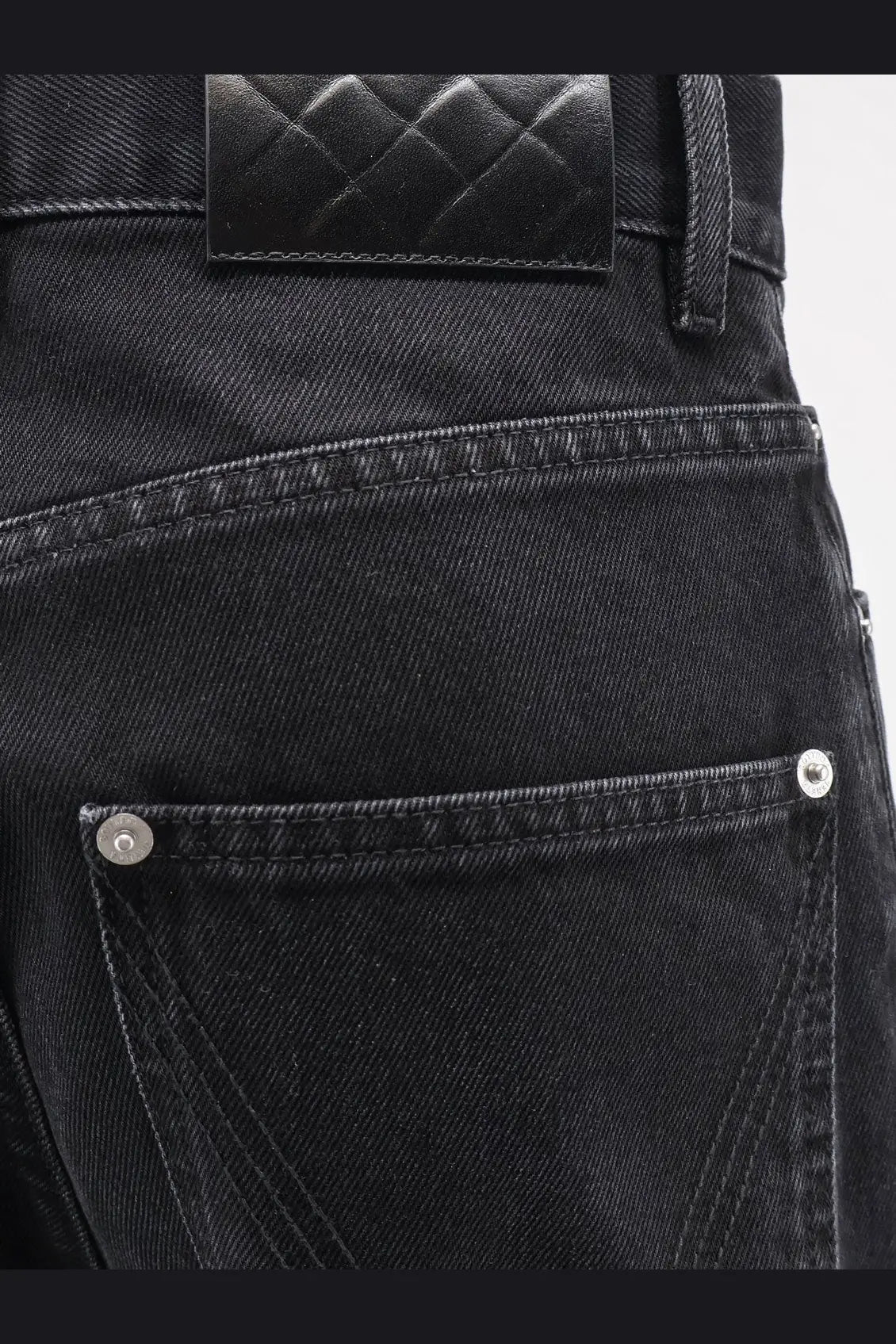 Back view of bottega veneta women’s black denim trousers with quilted leather waistband patch and silver rivets