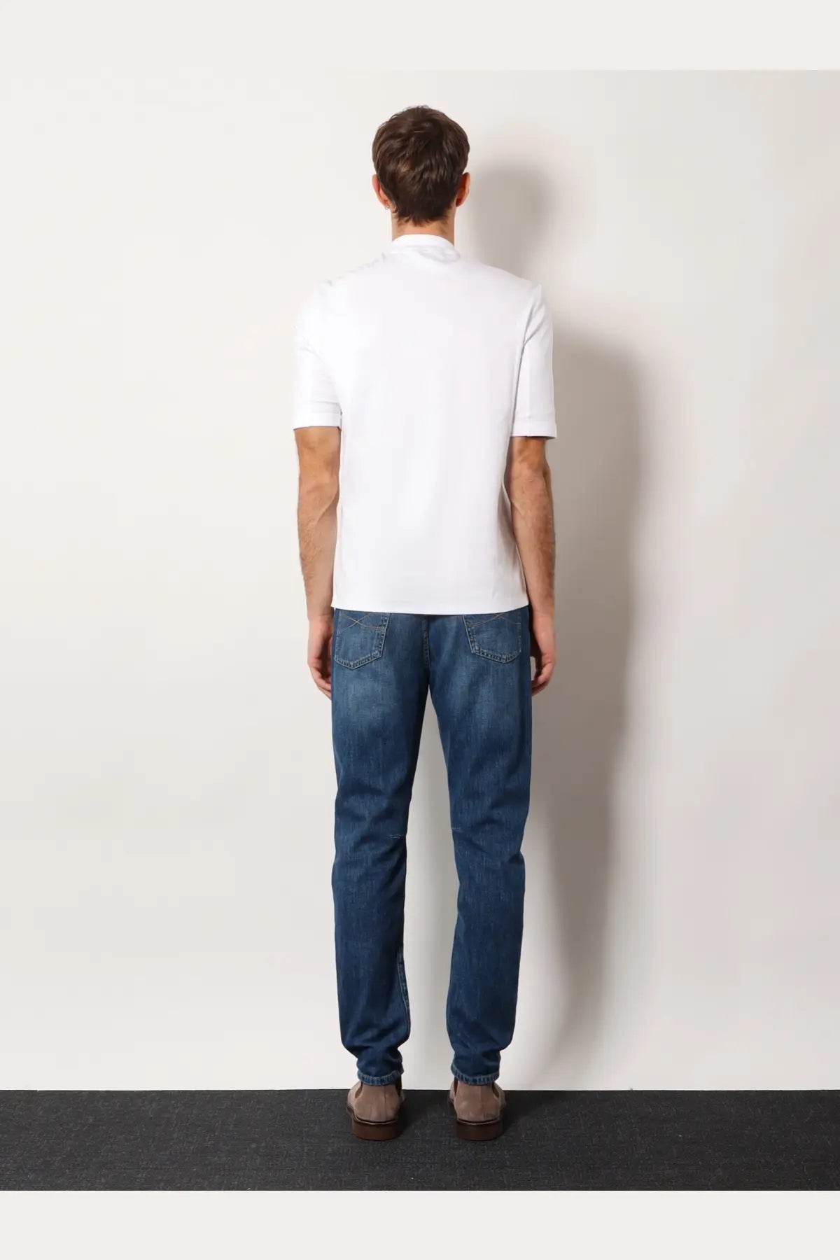 A man wearing a brunello cucinelli mens white cotton short-sleeved polo shirt with dark blue denim jeans