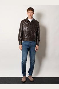 A sleek dark brown leather jacket with classic collar and two front flap pockets paired with brunello cucinelli blue cotton jeans