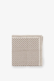A neatly folded brunello cucinelli men’s silk pocket square in beige with a subtle gray geometric pattern