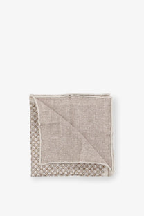 A neatly folded brunello cucinelli men’s silk pocket square in beige with a subtle geometric pattern and dark gray border