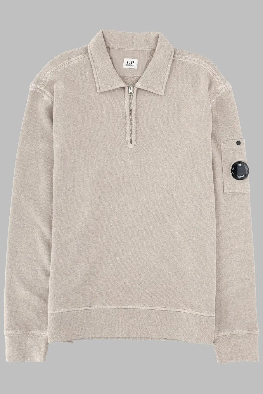 Beige textured knit polo shirt with half-zip front and black circular logo patch on the sleeve by C.P. Company