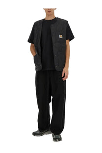 Black carhartt vest with multiple pockets and a small yellow logo on the chest paired with carhartt wip men’s belted pants black