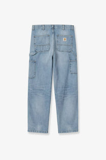 Back side of light-wash denim work pants with multiple pockets and carhartt logo patch on the back right pocket