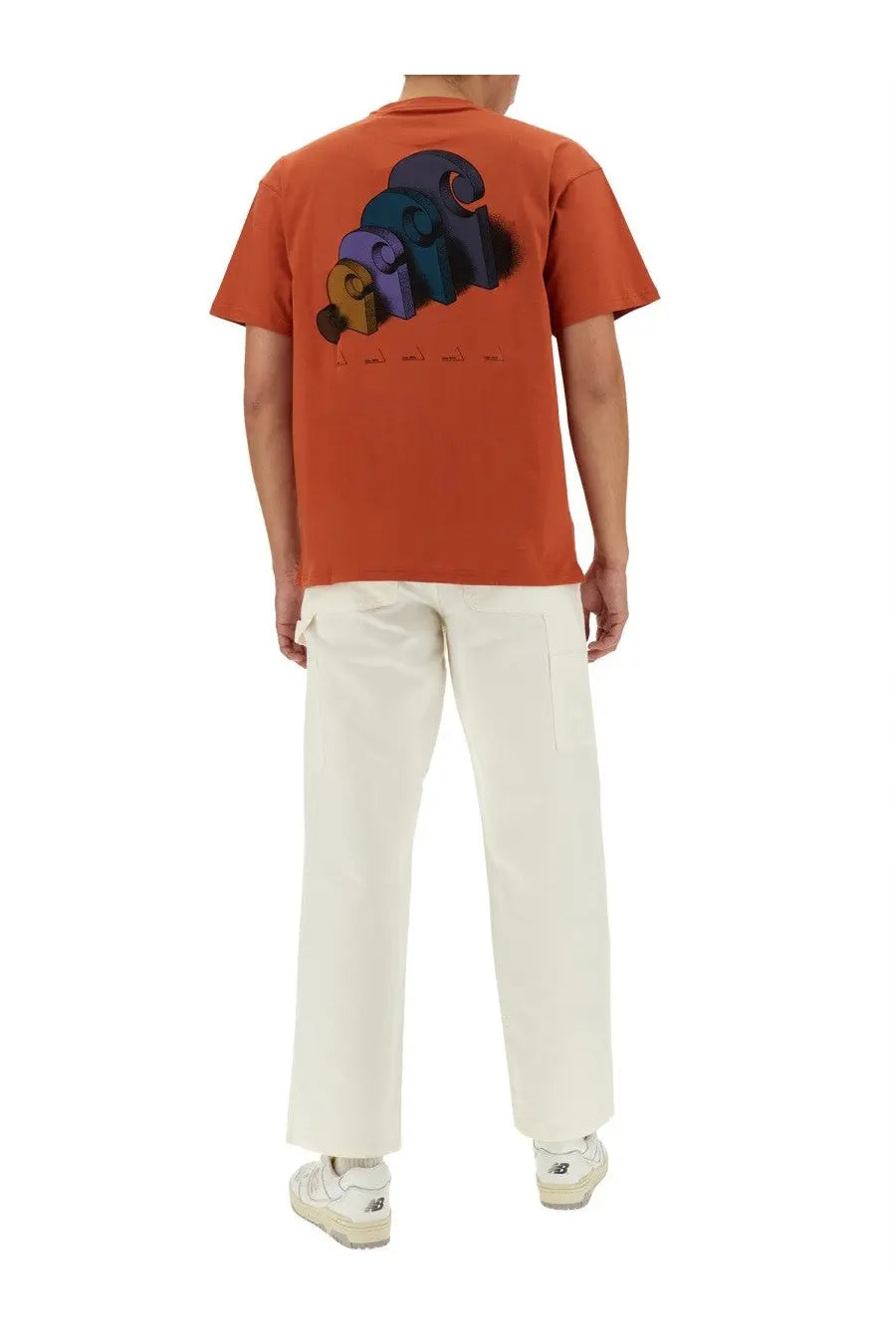 Back view of orange short-sleeved t-shirt with colorful 3d graphic print paired with white carhartt wip men’s pants