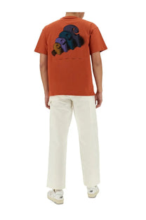 Back view of orange short-sleeved t-shirt with colorful 3d graphic print paired with white carhartt wip men’s pants