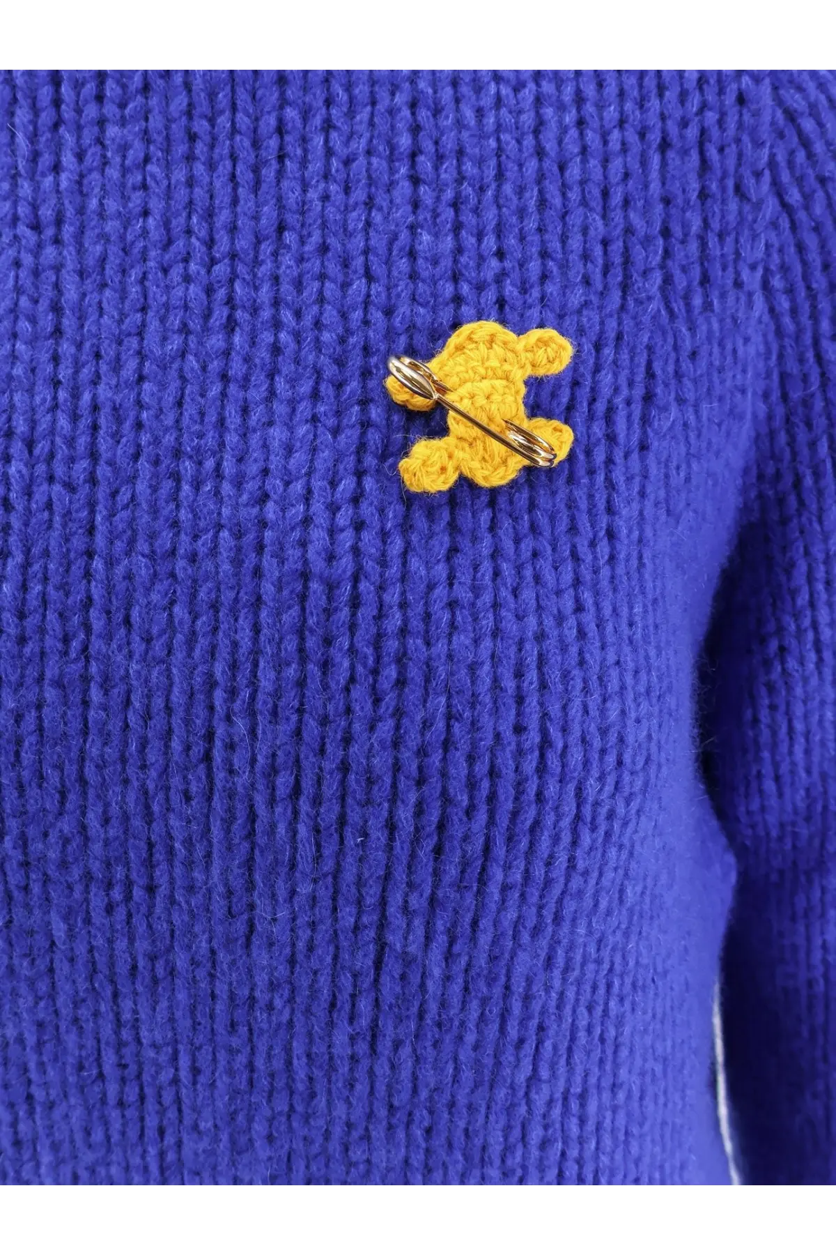 A yellow crocheted teddy bear pin with metallic clasp fastened to a vibrant blue celine women’s cashmere and silk blend sweater
