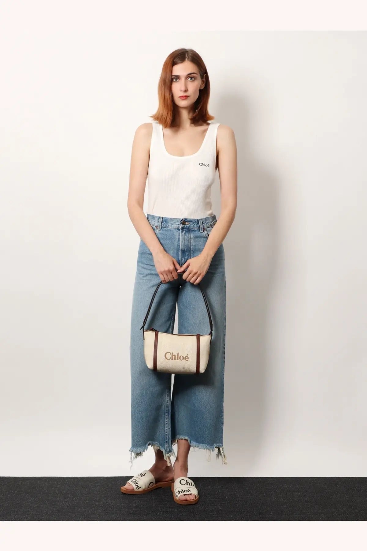 Cream-colored canvas handbag with brown leather trim black handles and chloé branding paired with white ribbed cotton tank top
