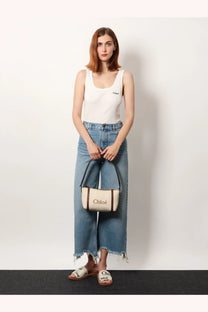 Cream-colored canvas handbag with brown leather trim black handles and chloé branding paired with white ribbed cotton tank top