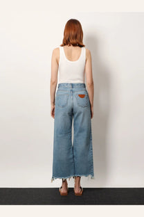 Light-wash denim wide-leg trousers with frayed hem and brown leather patch on back pocket shown from back view