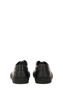 Back view of common projects men’s low-top black leather sneakers with gold branding on the heel