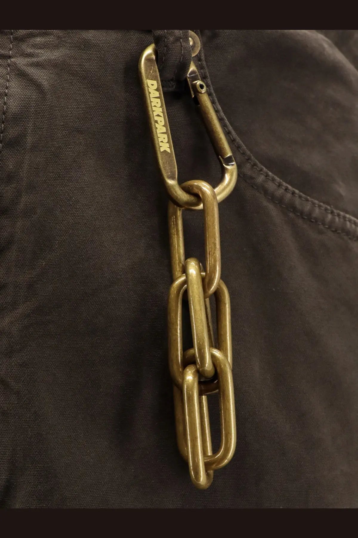 Darkpark men’s brown cotton trousers feature a brass-colored thick-link chain with a carabiner clip attached
