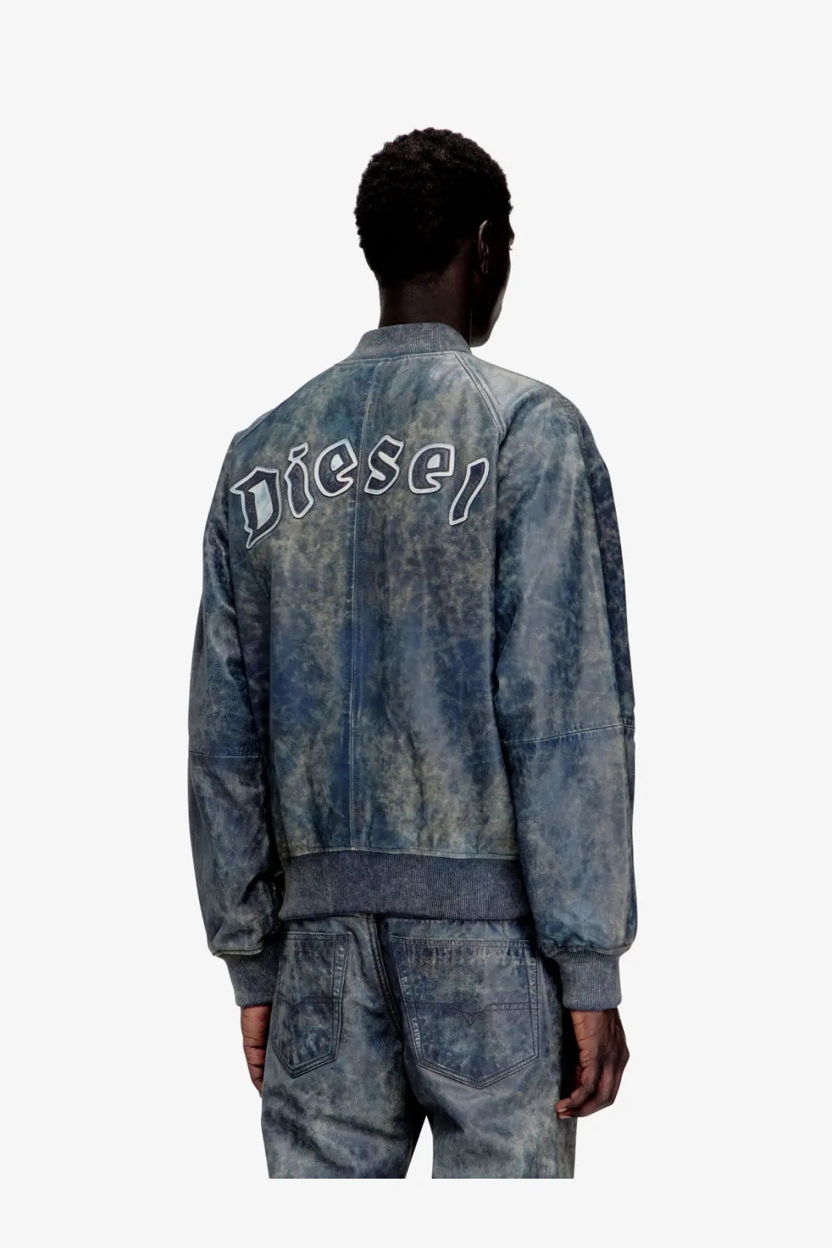 Back side of a blue denim bomber jacket with faded wash and diesel embroidered in white script across the back