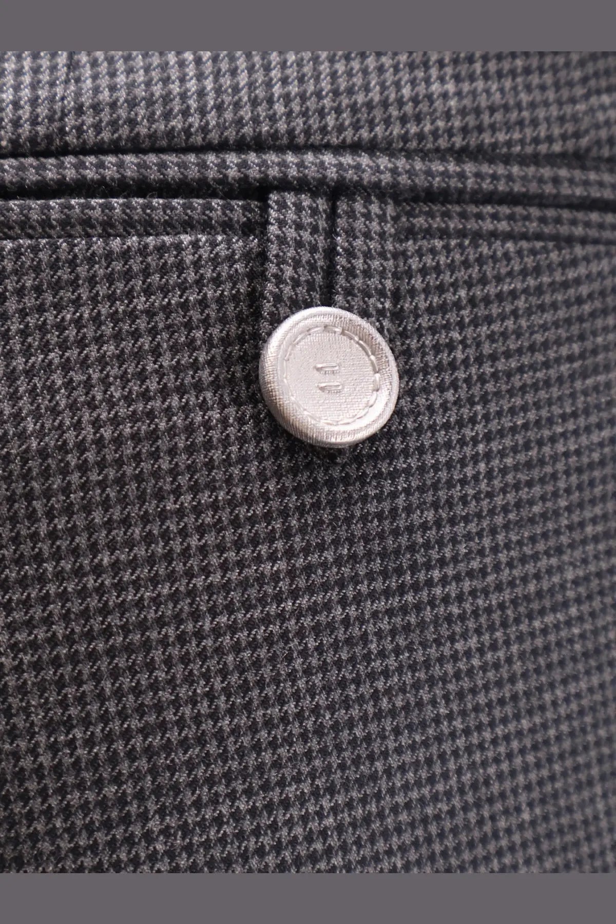 Silver button with textured surface on dior men’s grey cashmere and wool trousers set against dark gray herringbone fabric