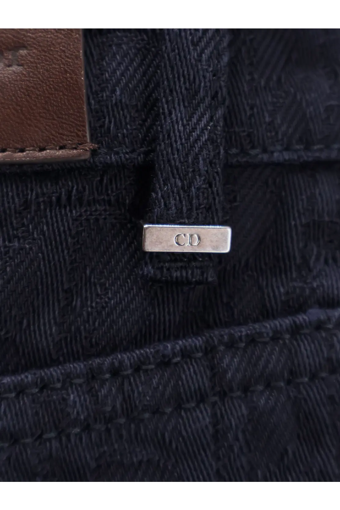 Silver rectangular metal tag with cd engraved attached to dark blue denim on back side of dior men’s cotton jeans