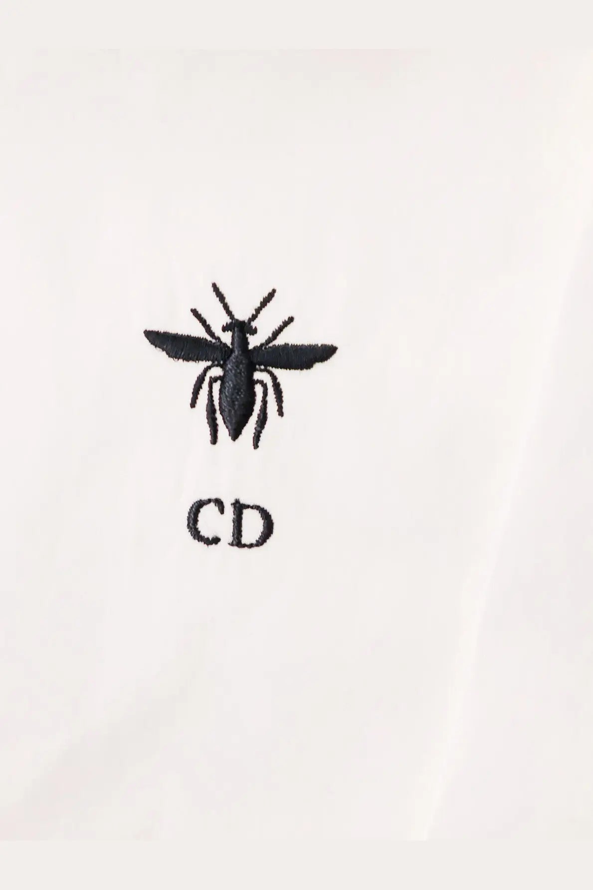 Black embroidered bee logo with cd initials on white fabric of dior women’s shirt front side