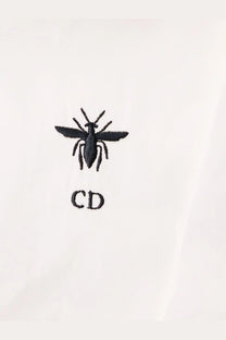 Black embroidered bee logo with cd initials on white fabric of dior women’s shirt front side