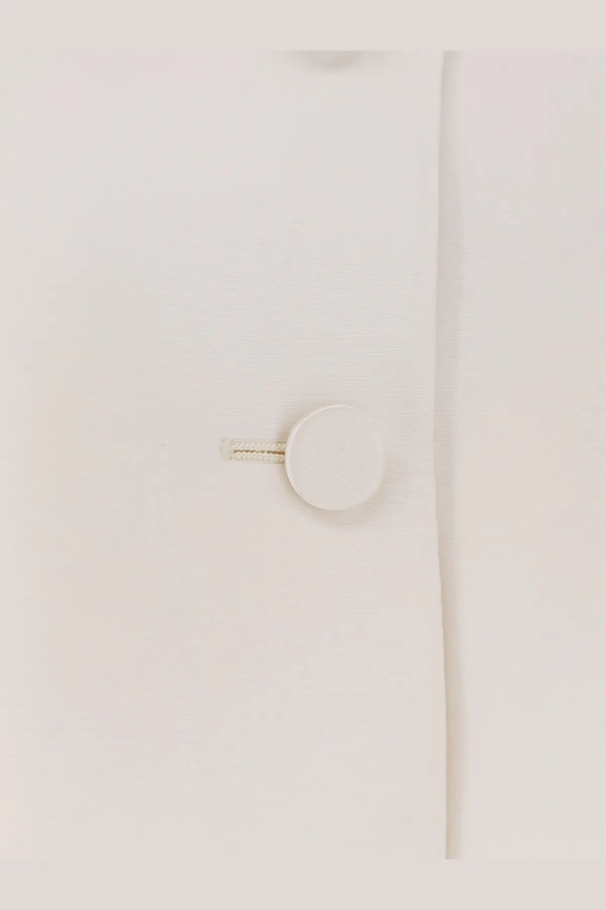 White circular button with metallic textured shank on light fabric of Dior women’s wool and silk blend jacket white