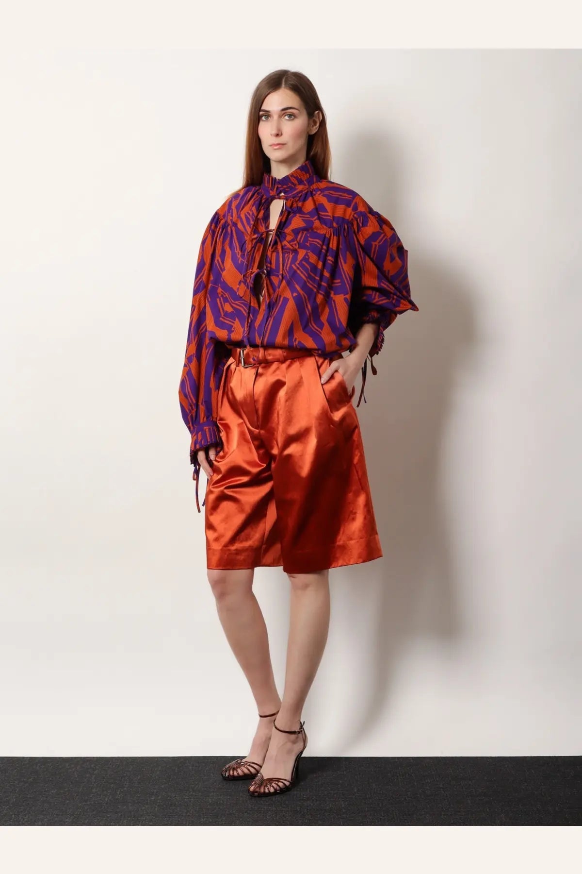 A vibrant orange satin high-waisted shorts with subtle pleats shown from the front, paired with dries van noten cotton shirt