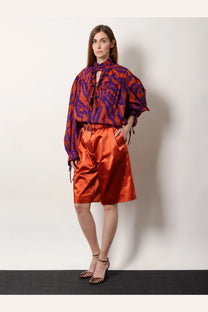 A vibrant orange satin high-waisted shorts with subtle pleats shown from the front, paired with dries van noten cotton shirt