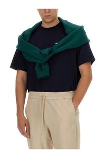 Dark green knitted sweater draped over shoulders with drôle de monsieur men’s blue cotton shirt visible underneath