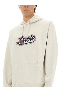 A light heather gray drôlé de monsieur men’s sweatshirt with bold brole logo embroidery and rose design accents