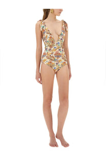 A woman wears an Etro women’s multicolor printed one piece swimsuit with deep v neckline and floral pattern on cream fabric