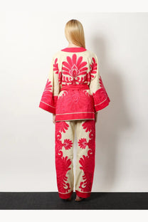 A woman wearing a cream kimono-style linen and viscose blend robe with red floral embroidery and pink trim from FARM Rio