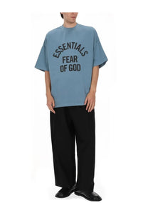 A light blue oversized fear of god essentials men’s shirt with bold black lettering across the chest