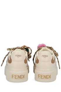 Fendi women’s beige match sneaker with cream leather, gold-tone branding, braided laces, and colorful pom-poms on tongue