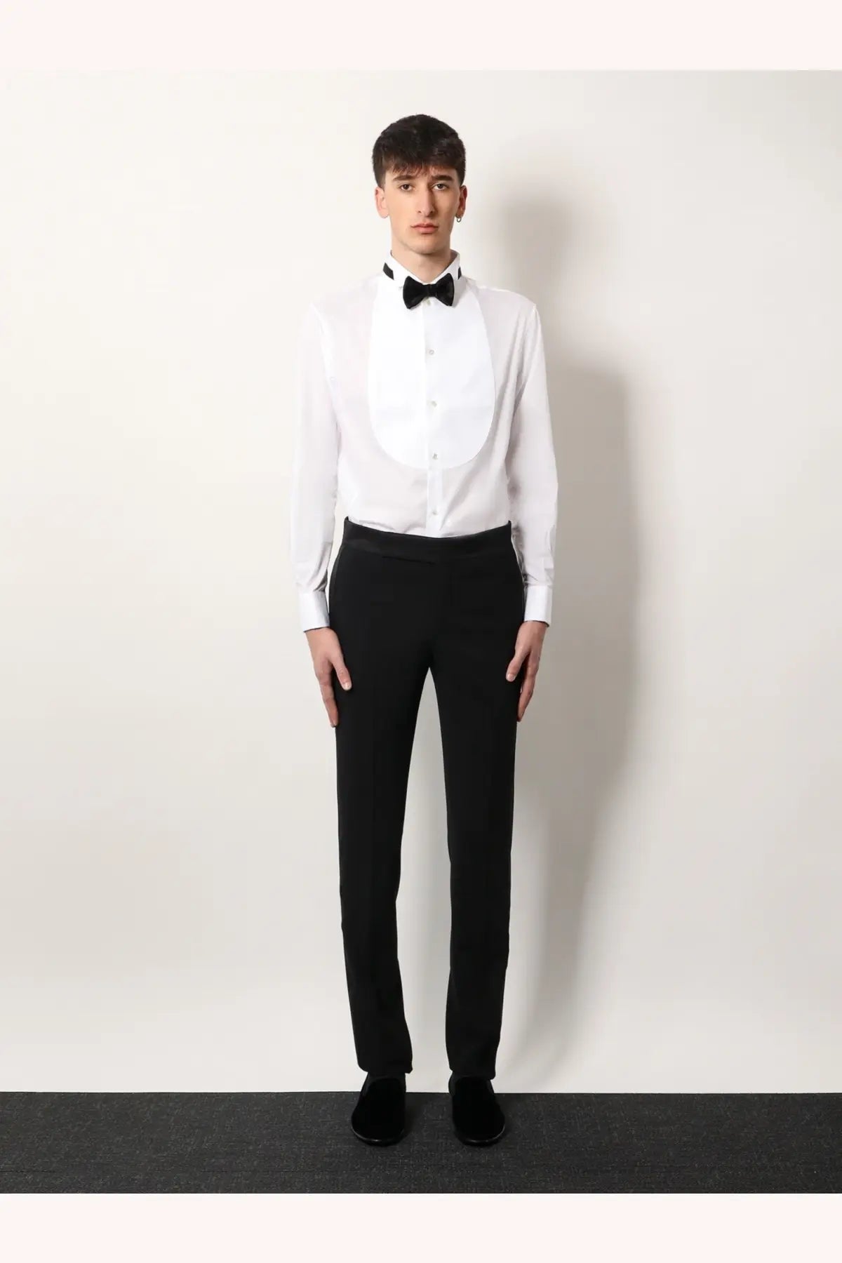 A man wearing a Giorgio Armani men’s white cotton tuxedo shirt with black bow tie and matching black trousers