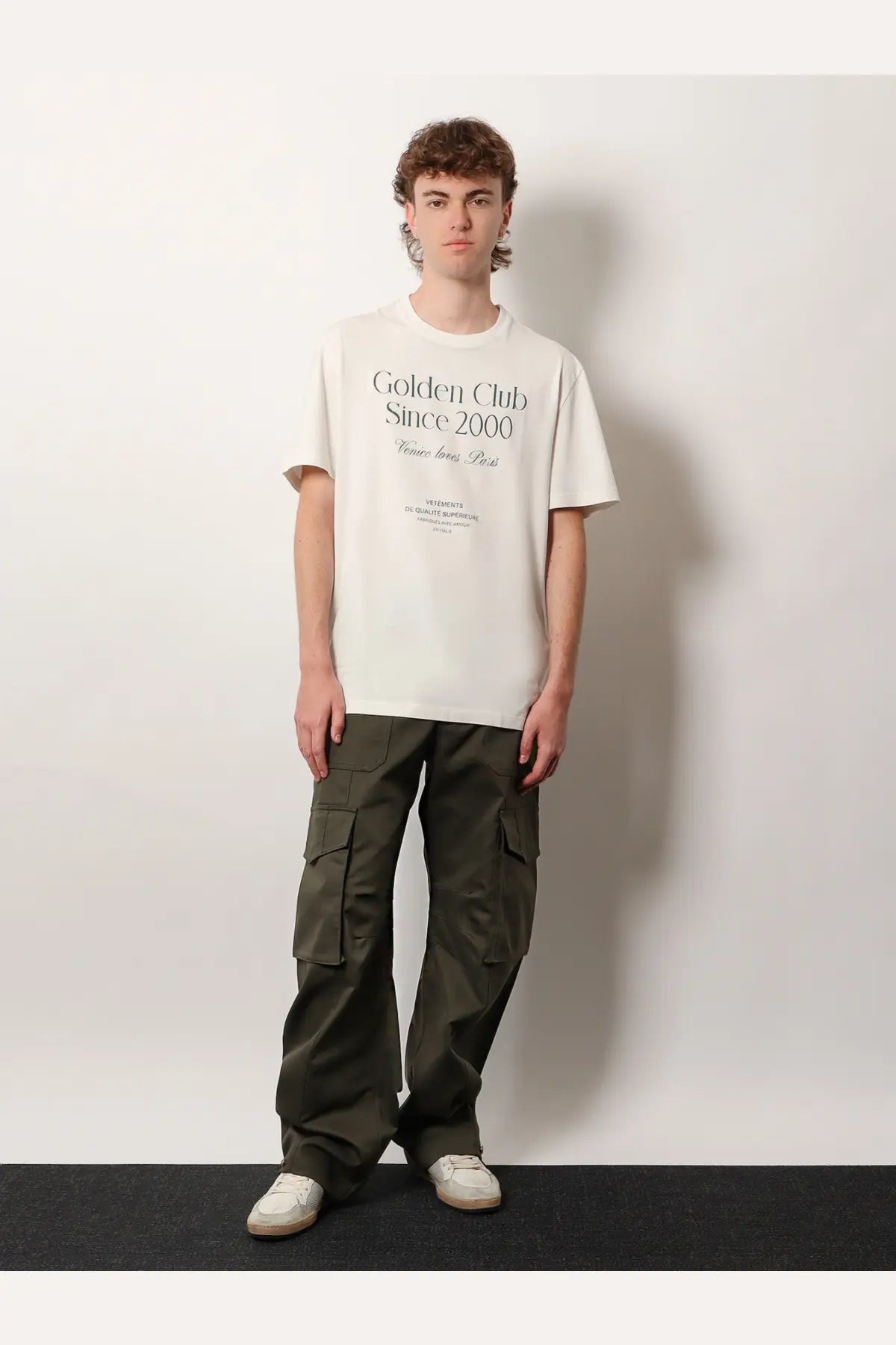 Off-white t-shirt with golden club since 2000 print in black serif font paired with golden goose green cotton blend trousers