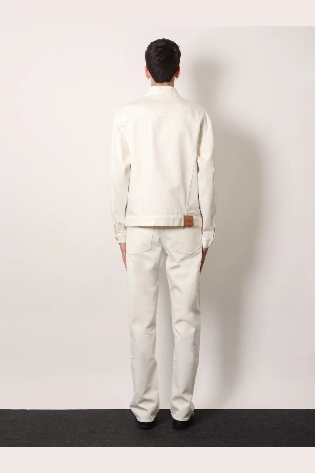 A crisp white denim jacket with a brown leather patch at the waistband shown from the back side