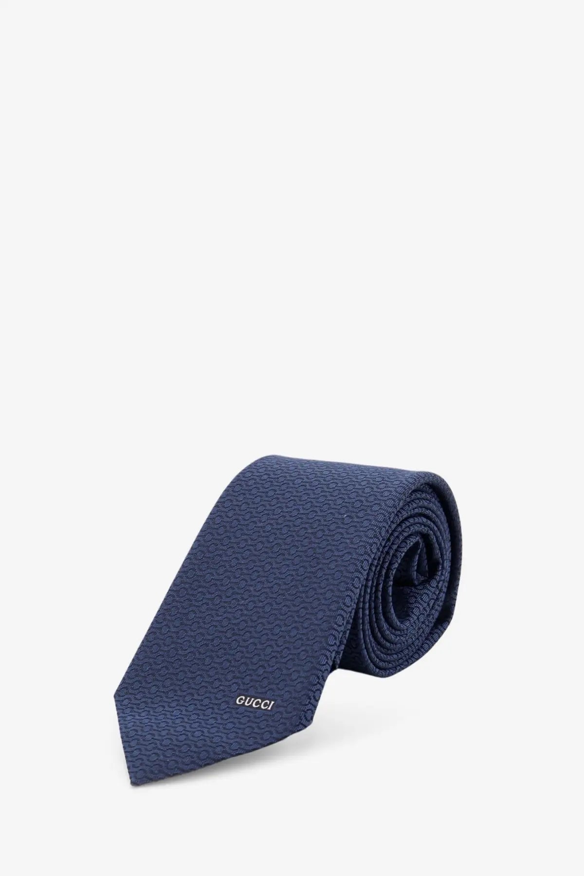 A navy blue gucci men’s silk tie with a subtle textured pattern and embroidered logo near the tip