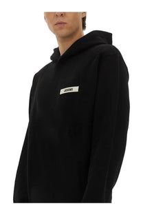 Jacquemus men’s black hooded sweatshirt with white rectangular label and black text on the chest