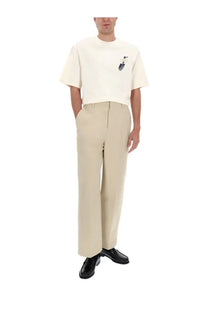 Cream-colored short-sleeved t-shirt with small embroidered graphic paired with jacquemus men’s pastro beige pants