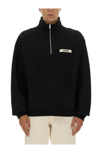 Black jacquemus men’s zippered turtleneck sweatshirt with silver zipper and white label on chest in jacobs mois fabric